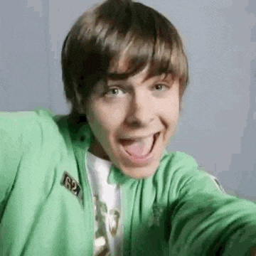 a young man in a green jacket is making a funny face with his tongue out .