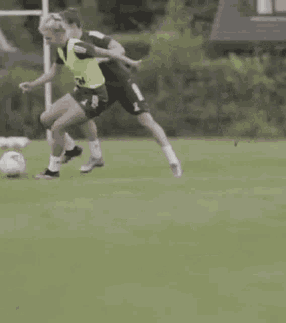 two soccer players are playing soccer on a field and one of them is wearing a yellow vest with the number 24 on it .