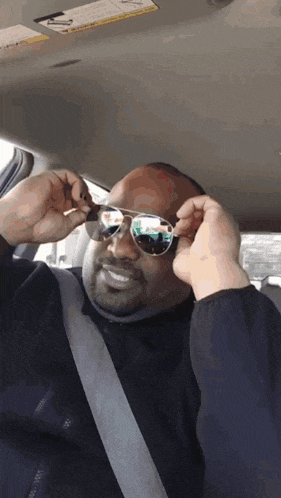 a man wearing sunglasses in a car with a seat belt on