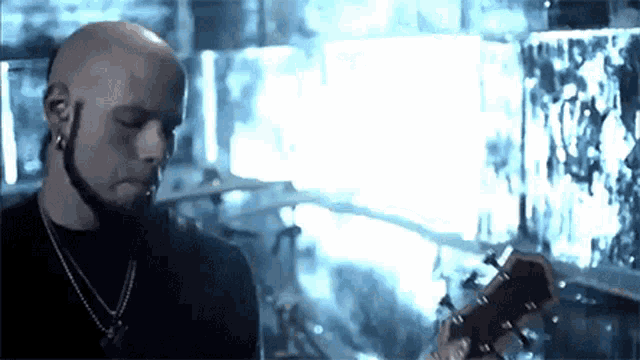 a bald man is playing a guitar in a dark room with a crowd in the background .