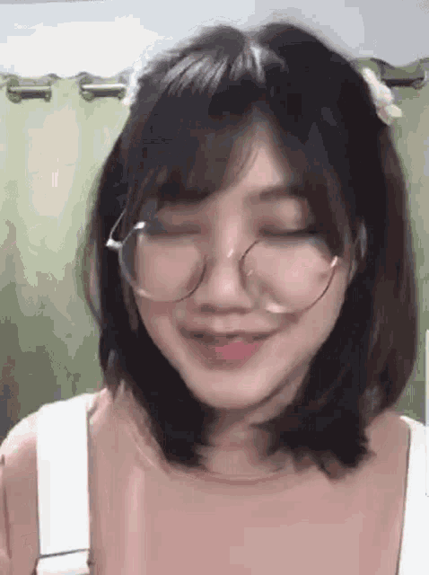 a girl wearing glasses and a flower in her hair is smiling with her eyes closed .