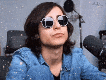 a young man wearing sunglasses and a denim jacket is sitting in front of a microphone ..