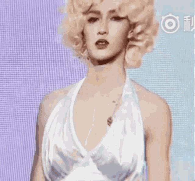 a man in a white dress and blonde hair is standing in front of a blue and purple background .