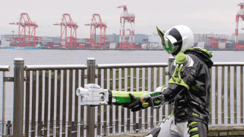 a man in a green and black costume is holding a gun in front of a body of water