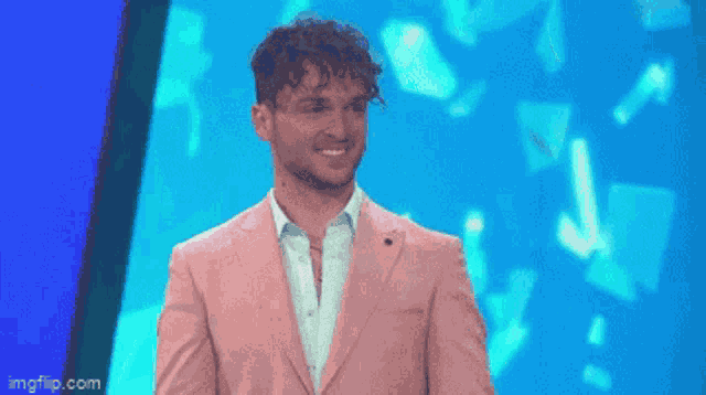 a man in a pink suit is standing in front of a blue background