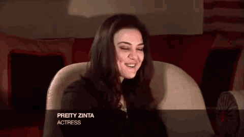 pretty zinta actress is smiling while sitting on a red couch