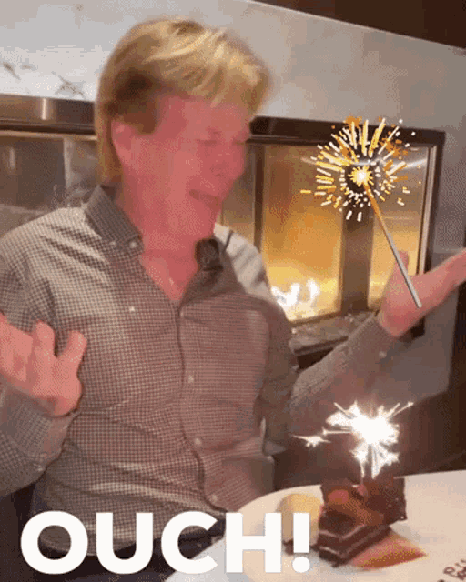 a man is holding a sparkler in front of a fireplace and the word ouch is on the bottom