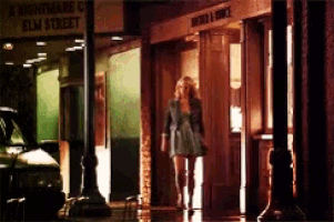 a woman is walking in front of a building that has a sign that says a nightmare on elm street