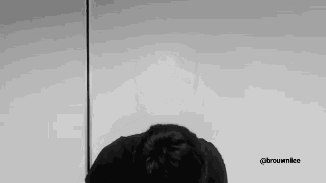a black and white photo of a person covering their face with their hands .