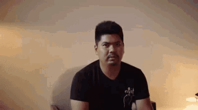a man in a black t-shirt is sitting in a chair and making a funny face .