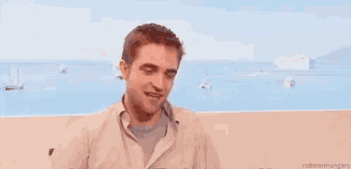 a man is sitting on a balcony overlooking the ocean and making a funny face with the word ouf written on the bottom