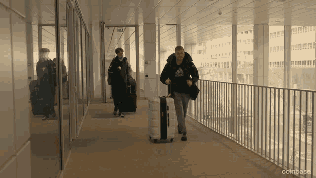 a man walking down a hallway carrying a suitcase with the word adidas on it