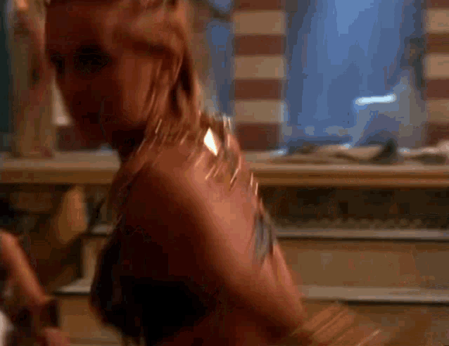 a woman in a black bra and gold jewelry is dancing in a dark room .