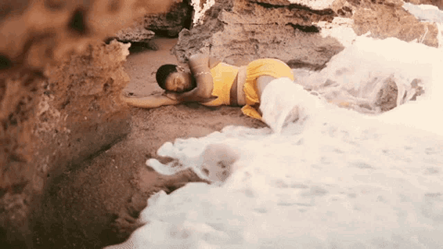 a woman in a yellow top is laying on a rocky beach