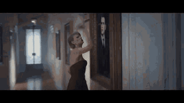 a woman in a red dress is looking at a painting of a man in a suit .