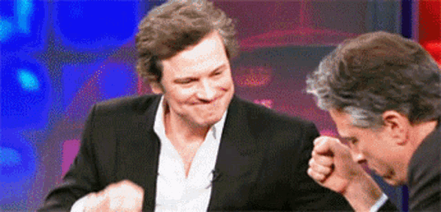 a man in a suit laughs while another man looks on