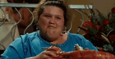 a woman in a blue shirt is sitting at a table eating a piece of pizza .