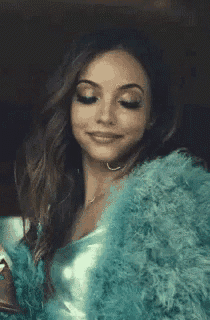 a woman wearing a blue fur coat and a metallic top is smiling .