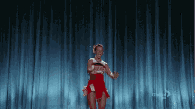 a cheerleader is standing on a stage in front of a blue curtain .