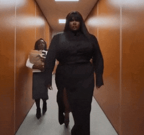 a woman in a black dress is walking down a hallway with another woman holding a magazine .