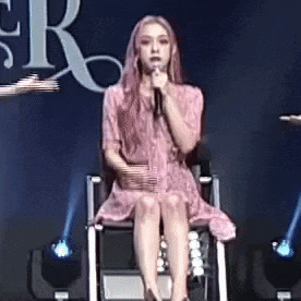 a woman in a pink dress is sitting in a wheelchair holding a microphone .