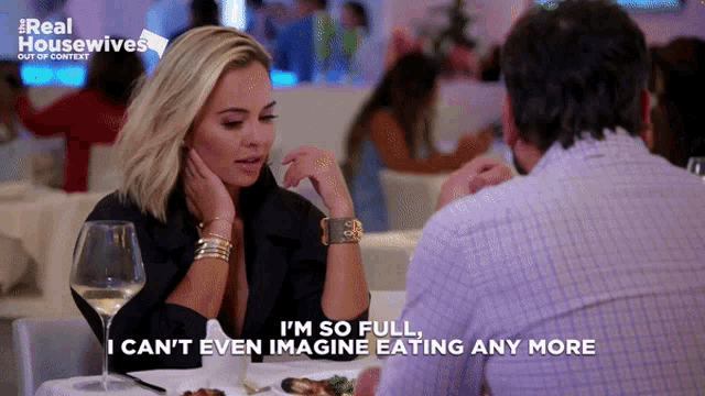 a woman is sitting at a table with a man and says i 'm so full i can 't even imagine