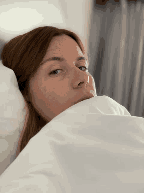 a woman laying in bed with her face covered by a white comforter