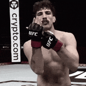 a man wearing a pair of ufc gloves stands in front of a crypto.com sign
