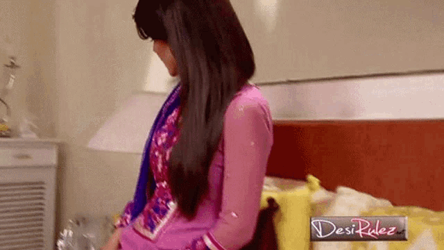 a woman in a pink dress is standing in front of a bed with a desi rulez logo