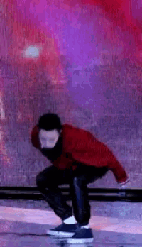 a man in a red sweater is squatting down in front of a pink and purple background .