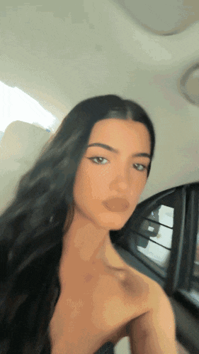 a woman with long hair is taking a selfie in a car .