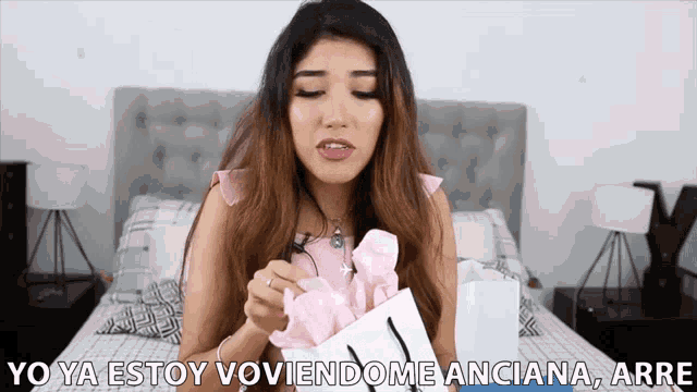 a woman in a pink dress is holding a gift bag and says yo ya estoy