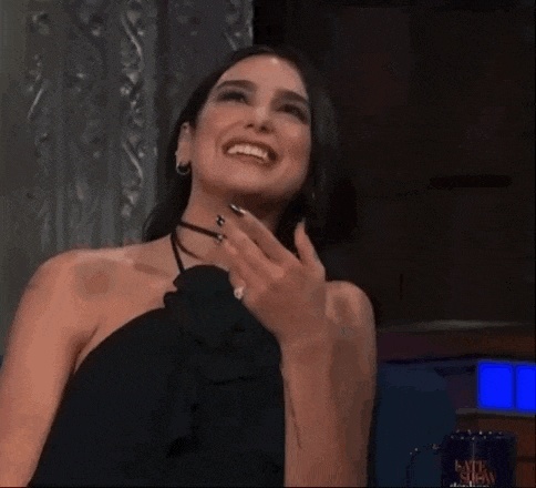 a woman in a black dress is smiling with her hand on her face