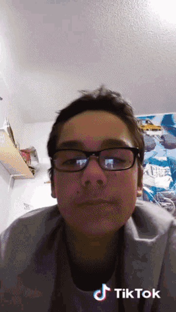 a boy wearing glasses and a grey shirt has a tik tok sticker on his face