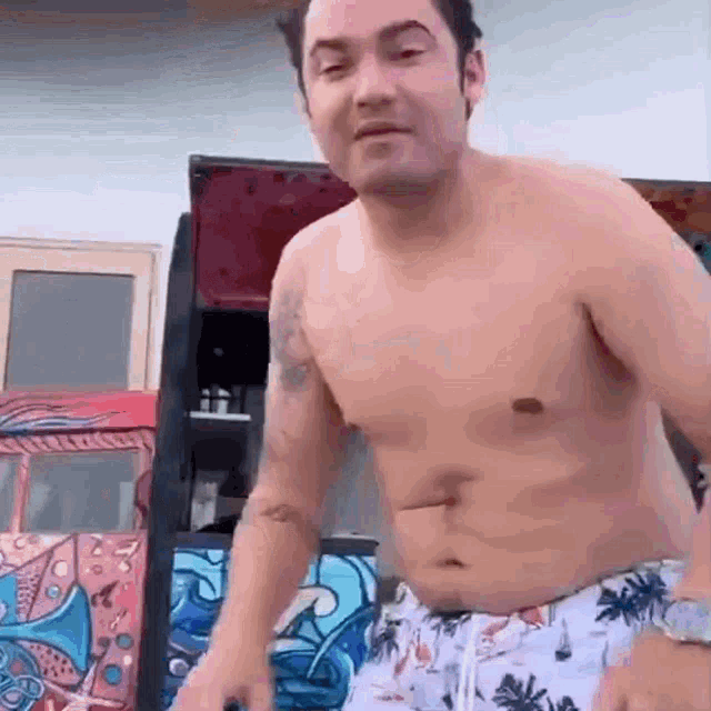 a shirtless man in a pair of swim trunks is standing in front of a graffiti wall .