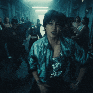 a group of people are dancing in a dark hallway with a man wearing a blue jacket