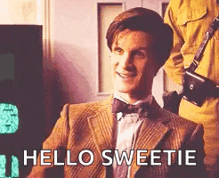 a man in a suit and bow tie is smiling and says `` hello sweetie '' while holding a camera .
