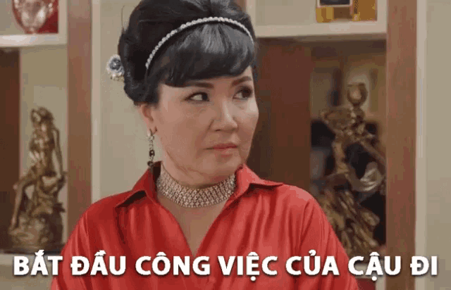 a woman wearing a red shirt and a choker stands in front of a sign that says " bat dau cong vien cua cau di "