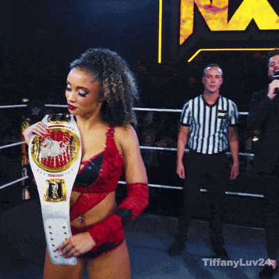a woman in a red dress is holding a championship belt in a ring
