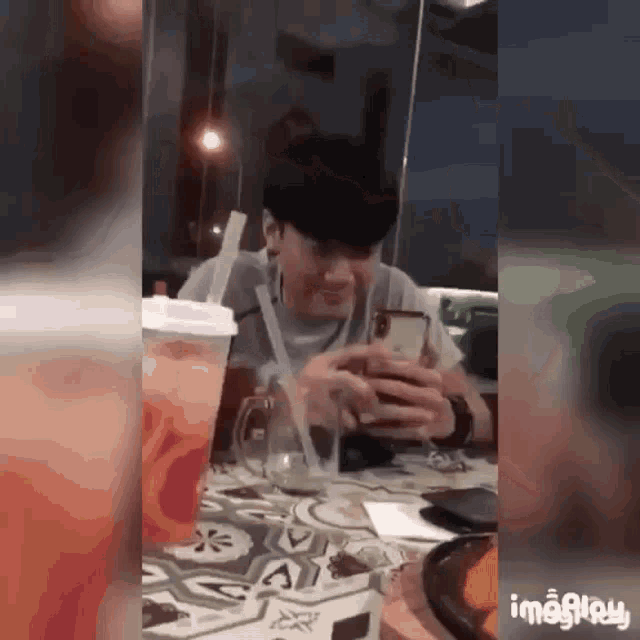 a man is sitting at a table with a straw in his mouth and looking at his phone .