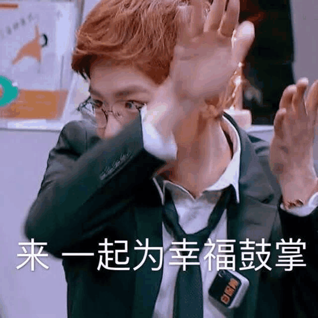 a man in a suit and tie is covering his face with his hands and making a funny face .