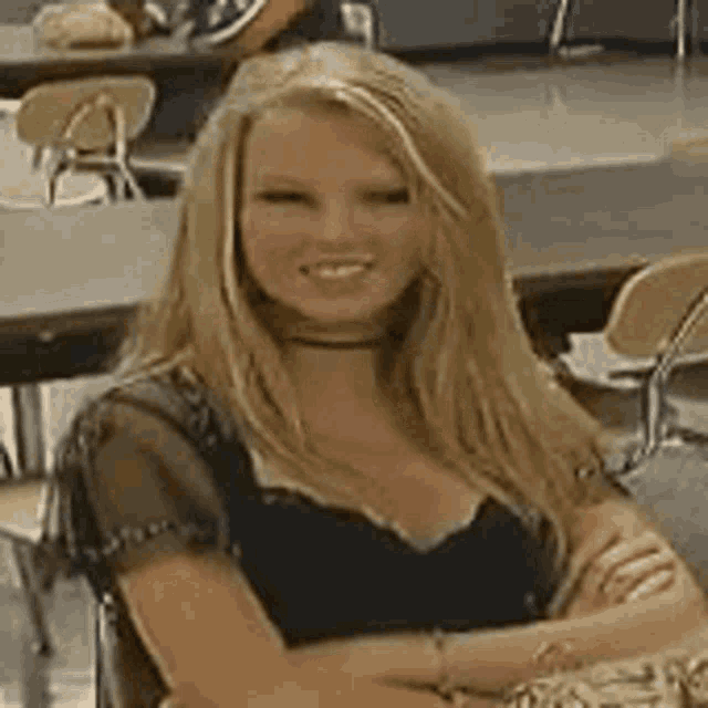 a woman with long blonde hair is sitting at a table with her arms crossed and smiling .