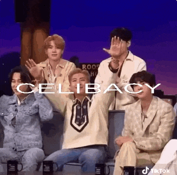 a group of men are sitting in a row on a stage with their hands up in the air .