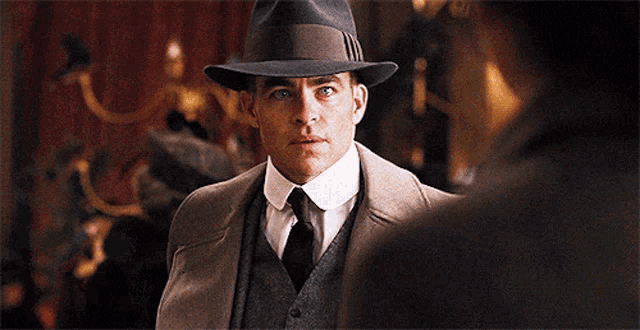 a man wearing a hat and a suit stands in front of another man
