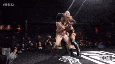 two women are wrestling in front of a crowd with the hashtag #jbbs12 on the screen