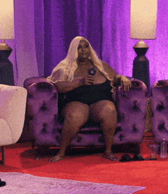 a woman sits in a purple chair with a microphone in her hand