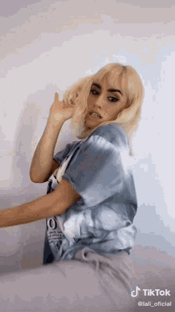 a woman with blonde hair is wearing a blue tie dye shirt and grey shorts