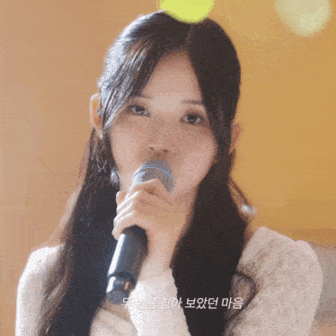 a girl singing into a microphone with korean writing on the bottom right