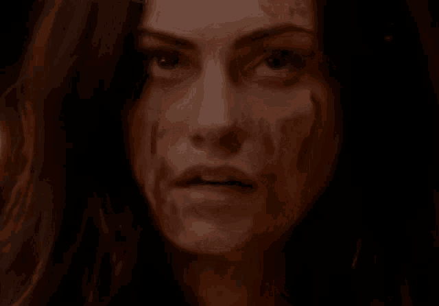 a woman with blood on her face is looking at the camera in a dark room .