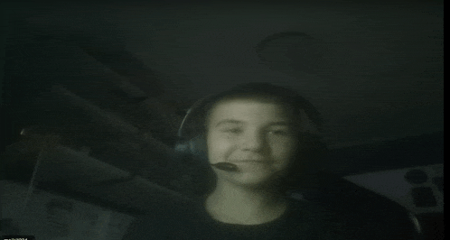 a young boy wearing headphones and a microphone looks at the camera in a dark room